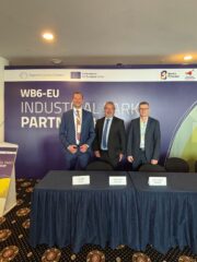 Drei Männer stehen hinter einem Tisch bei der WB6-EU Industrialpark-Partnerschaft Konferenz mit EU-Logos.