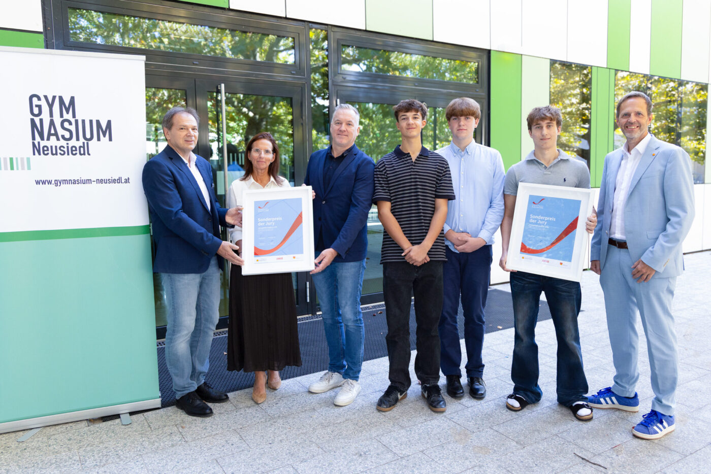 Gymnasium Neusiedl Schüler und Lehrer präsentieren Sonderpreis vor Schulgebäude mit grüner Fassade