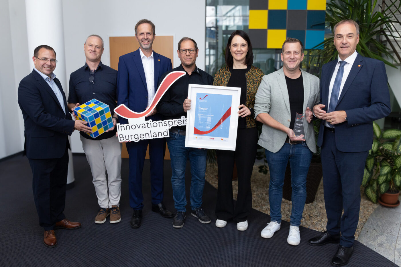 Innovationspreis Burgenland Gewinner: Sieben Personen präsentieren Preis und Urkunde in modernem Büro.