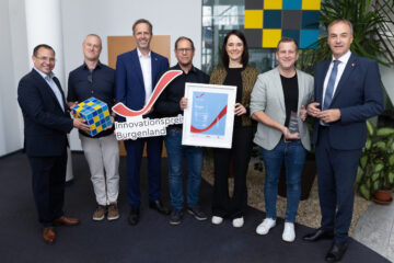 Innovationspreis Burgenland Gewinner: Sieben Personen präsentieren Preis und Urkunde in modernem Büro.