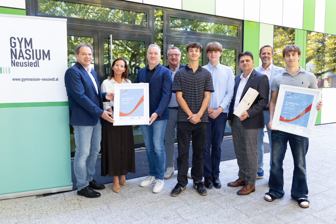 Gymnasium Neusiedl Preisverleihung mit Schülern und Lehrern vor dem Schulgebäude mit Auszeichnungen. (_r6a8701_innovationspreis-wab)