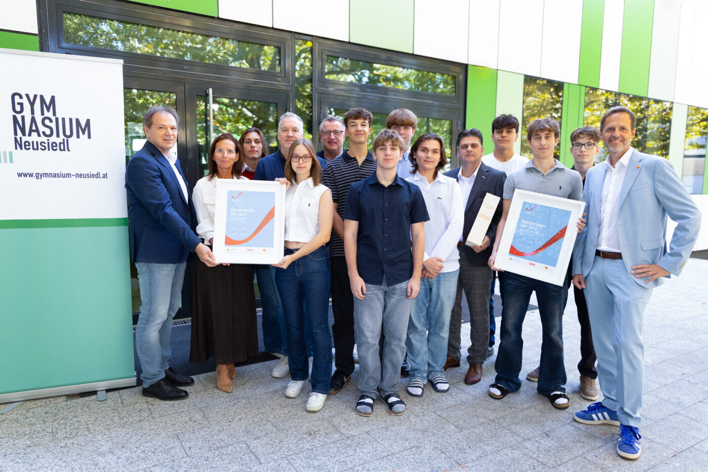 Gymnasium Neusiedl Team mit Schülern und Lehrern hält Auszeichnungen vor dem Schulgebäude (_r6a8712_innovationspreis_wab)