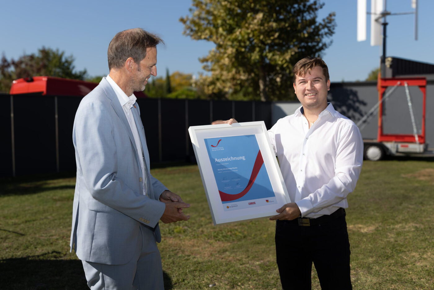 Auszeichnung Übergabe: Zwei Geschäftsmänner in weißen Hemden halten Urkunde im Freien vor Industriegelände. (_r6a8726_innovationspreis-wab)