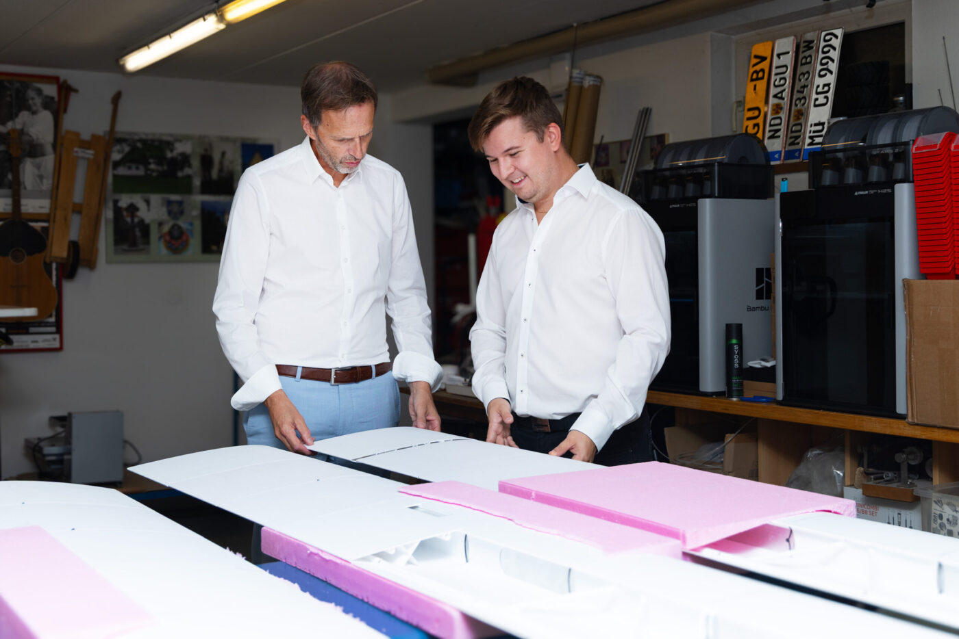 Zwei Männer in weißen Hemden besprechen Druckproben und Materialien an einem Tisch in einer Druckerei. (_r6a8780_innovationspreis-wab)