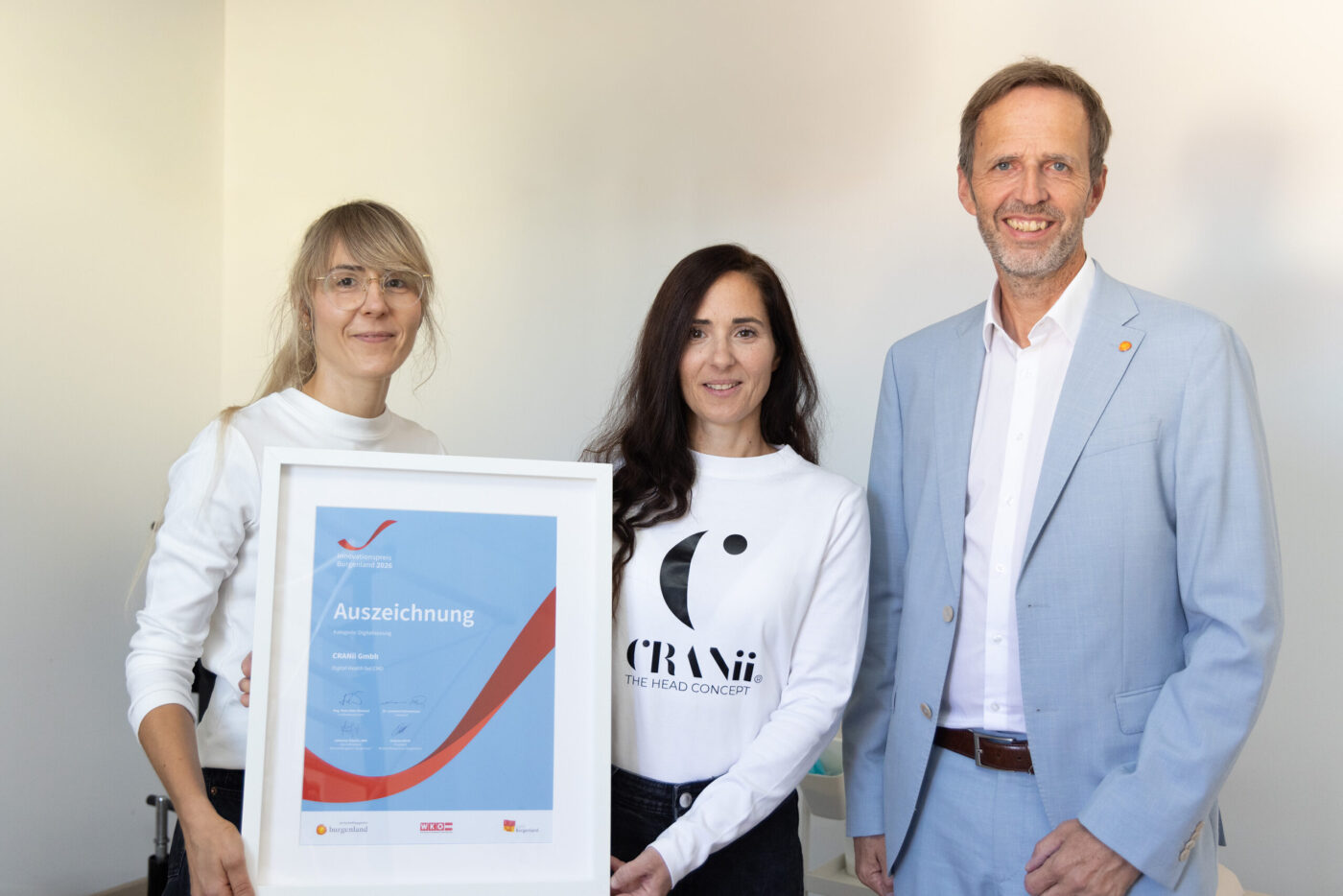 Drei Personen präsentieren eine Auszeichnung für CRANiO GmbH vor neutralem Hintergrund. (_r6a8858_innovationspreis-wab)