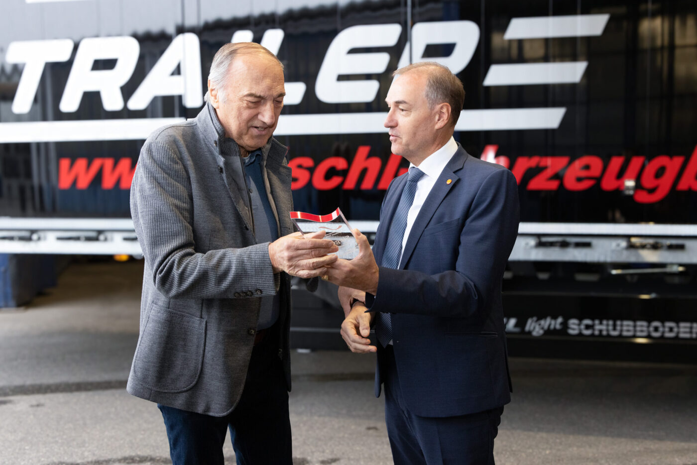 Zwei Geschäftsmänner in Anzügen übergeben ein Zertifikat vor einem Schubodener Trailer bei einer Geschäftsveranstaltung. (_r6a9095_inovationspreis_wab)