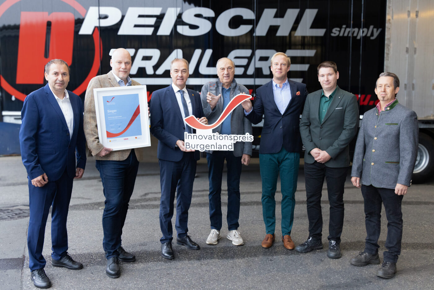 Peischl Trailer gewinnt Innovationspreis Burgenland, sieben Männer posieren vor Firmengebäude mit Auszeichnung. (_r6a9111_innovationspreis_wab)